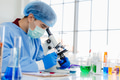 Asian male researcher in laboratory or chemist notes while studying virus sample using microscope - PhotoDune Item for Sale