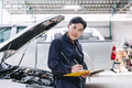 Happy Asian Mechanic young male staff worker working with car engine front hood auto service check t - PhotoDune Item for Sale