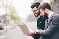two businessman sitting outdoors business district using sharing computer smiling - PhotoDune Item for Sale