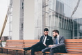Two young elegant businessmen sitting outdoors bench discussing - PhotoDune Item for Sale