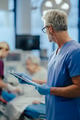 Mature male doctor looking at patient in hospital bed. ER doctor examining senior patient, reading - PhotoDune Item for Sale