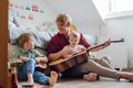 Father teaching boys to play on guitar. Boys having fun in their room with dad, playing guitar and - PhotoDune Item for Sale