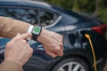 Close up of businessman with smartwatch, checking charging of his electric car. - PhotoDune Item for Sale