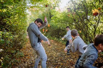 Father with his kids having fun in forest, throwing foliage.