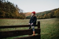 Young girl in warm clothes sitting on aged wooden fence, wooden gate, looking at autumn nature. - PhotoDune Item for Sale