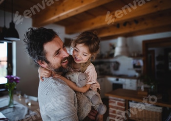 Mature father with small daughter standing indoors at home, holding and hugging