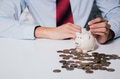 Businessman in formal suit putting and inserting coins in piggy bank with calculator - PhotoDune Item for Sale