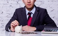 Businessman in formal suit putting and inserting coins in piggy bank with calculator nearby - PhotoDune Item for Sale