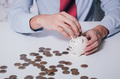 Businessman in formal suit putting and inserting coins in piggy bank with calculator nearby - PhotoDune Item for Sale