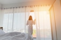 Back view of female in bathrobe touching curtains and looking out window while standing in stylish - PhotoDune Item for Sale