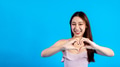 Happy smiling Asian female stylish woman making a heart hand gesture isolated in blue background - PhotoDune Item for Sale