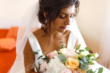Morning of bride. Beautiful smiling brunette bride in white dress with wedding bouquet in her hands.