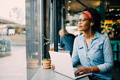 Smiling young African woman working online by a cafe window - PhotoDune Item for Sale