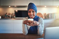 Smiling young Arabic woman sitting in her kitchen drinking coffee - PhotoDune Item for Sale