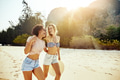 Two young women laughing while walking along a sandy beach - PhotoDune Item for Sale