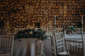 Elegant, romantic table setting for indoor wedding reception with fairy lights on wall behind - PhotoDune Item for Sale