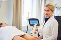 Smiling clinic technician performing electrolysis on a female client's leg - PhotoDune Item for Sale