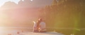 Rear View Of Loving Couple Sitting On Wooden Jetty By Lake At Sunset With Lens Flare - PhotoDune Item for Sale