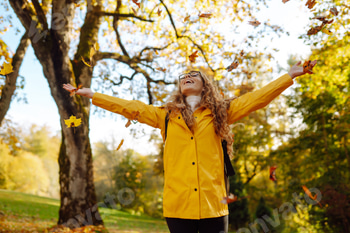 Happy female hiker in yellow coat walking in golden autumn forest. Woman has fun in autumn in park.