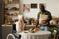 Senior Caucasian Woman with Disability Smiling While Black Man Bringing Groceries - PhotoDune Item for Sale