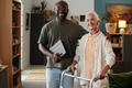 Portrait of Black Man Supporting Senior Caucasian Woman Using Walker Indoors - PhotoDune Item for Sale
