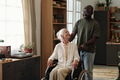 Black Man Assisting Senior Caucasian Woman Using Wheelchair Indoors - PhotoDune Item for Sale