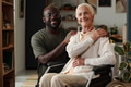Portrait of Senior Caucasian Woman in Wheelchair with Disability Smiling with Young Black Man - PhotoDune Item for Sale