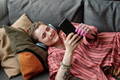 Young Caucasian Woman Wearing Headphones Lying on Sofa Using Smartphone - PhotoDune Item for Sale
