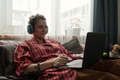 Young Caucasian Woman Using Laptop and Headphones While Sitting on Bed - PhotoDune Item for Sale