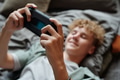 Teenage Caucasian Boy Lying on Bed Using Smartphone and Displaying Gadget Addiction - PhotoDune Item for Sale