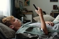 Teenage Caucasian Boy Lying on Bed Using Smartphone and Experiencing Gadget Addiction - PhotoDune Item for Sale