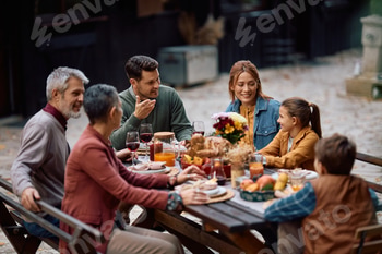 Happy multi-generation family talking while having Thanksgiving meal on the patio.