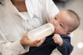 Mother feeding baby with milk bottle indoors - PhotoDune Item for Sale