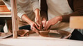 Close Up Of Female Teacher Helping Man Sitting At Wheel In Pottery Class - PhotoDune Item for Sale