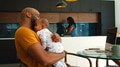 Father Cuddling Baby Daughter As Mother Works In Kitchen - PhotoDune Item for Sale