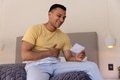 Young man sitting on bed smiling while holding and looking at photograph - PhotoDune Item for Sale