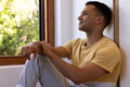 Young man sitting by window, enjoying peaceful moment at home - PhotoDune Item for Sale