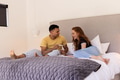 Young couple sitting on bed, smiling and holding pregnancy test together - PhotoDune Item for Sale