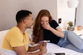 Young couple on bed holding pregnancy test, expressing surprise and joy together - PhotoDune Item for Sale