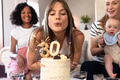 Woman blowing out candles on birthday cake while friends celebrate at home - PhotoDune Item for Sale
