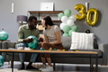 Celebrating 30th birthday, couple laughing with balloons on living room sofa - PhotoDune Item for Sale