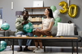 Friends celebrating 30th birthday at home, inflating balloons and smiling joyfully - PhotoDune Item for Sale