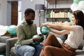 Friends laughing and inflating balloons on sofa during festive celebration at home - PhotoDune Item for Sale