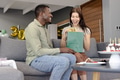 Couple exchanging gifts on sofa, celebrating birthday with cake and balloons - PhotoDune Item for Sale