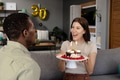 Woman holding birthday cake with candles, smiling at man in living room - PhotoDune Item for Sale