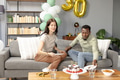 Celebrating birthday, friends enjoying cake and snacks on cozy living room sofa - PhotoDune Item for Sale