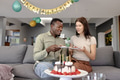 Celebrating birthday, couple enjoying cake together on living room sofa - PhotoDune Item for Sale
