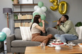 Friends celebrating 30th birthday at home, blowing party horns on sofa - PhotoDune Item for Sale