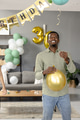 Smiling man holding gold balloon celebrating birthday at home with decorations - PhotoDune Item for Sale