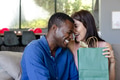 Couple laughing together while exchanging gift bag at home, enjoying special moment - PhotoDune Item for Sale